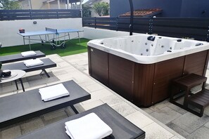 Une terrasse extérieure avec un jacuzzi, des tables et des chaises.