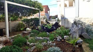 En have med forskellige planter, sten og en hvid bygning.