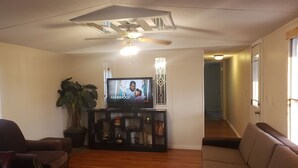 A living room with a television, a ceiling fan, a potted plant, and a staircase leading to another room. - THE LIONS DEN  Home Next to  Lion & Tiger Reserve (Burlington)