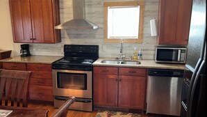 A kitchen with wooden cabinets, a stainless steel stove, a microwave, and a dishwasher. - THE LIONS DEN  Home Next to  Lion & Tiger Reserve (Burlington)