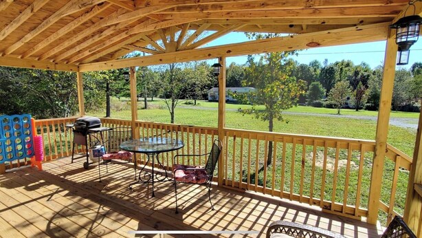A covered outdoor deck with a table and chairs, a grill, and a blue play structure. - THE LIONS DEN  Home Next to  Lion & Tiger Reserve (Burlington)