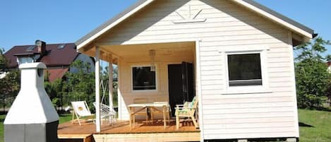 A small, single-story wooden cabin with a porch, a table, and two chairs.