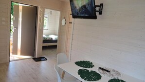 Una stanza con un letto, un tavolo con motivo a foglia decorativa, un televisore fissato al muro e una porta che dà su un'altra stanza.