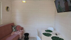 Una stanza accogliente con una parete in legno, un tavolo bianco decorato con foglie e un divano rosa, oltre a uno sgabello nero.
