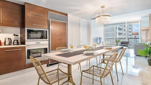A modern kitchen with wooden cabinets, stainless steel appliances, and a dining area with a white table and wicker chairs.