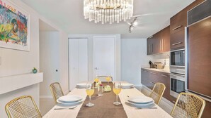 A modern kitchen with stainless steel appliances, a dining area with a long table and chairs, and a chandelier.