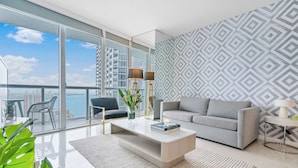 A modern living room with a large window, a grey sofa, a coffee table, and a patterned wall.