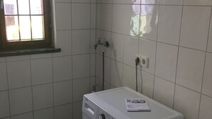 A compact laundry room with a front-loading washing machine, a small window, and tiled walls.