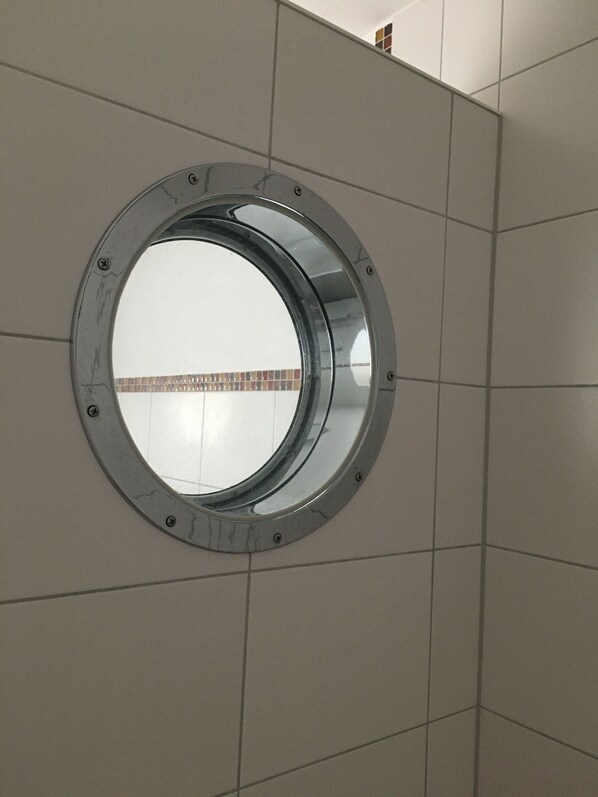 A circular window with a metal frame, set in a tiled wall.