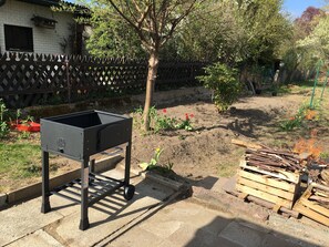 A barbecue grill in a backyard with a wooden fence, a tree, and a pile of firewood.