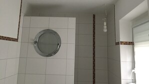 A bathroom with white tiles, a round mirror, a green basket, and a light fixture.