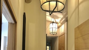 Un couloir avec une porte en bois, un miroir à cadre noir, une sculpture en bois et un luminaire suspendu.