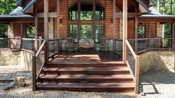 Eine Holzhütte mit Veranda, Steinmauern und Blick ins Waldgebiet.