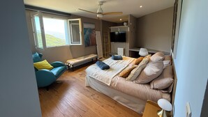 Ein Schlafzimmer mit einem Bett, einer Bank, einem Sessel, einem Fernseher und einem Deckenventilator.
