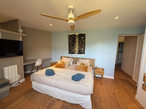 Ein Schlafzimmer mit einem Bett, einem Deckenventilator, einem Fernseher, einem Sessel und einem Bild an der Wand.