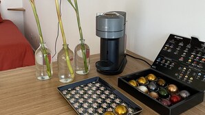 A wooden table with a coffee maker, two glass vases with flowers, a tray of coffee capsules, and a menu stand. - L'Oasis de Saint-Jacques (SAINT DENIS)