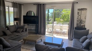 Una sala de estar moderna con un sofá gris, un televisor de pantalla plana, una mesa de centro y un balcón con mobiliario exterior.
