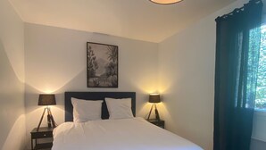 Un dormitorio con cama, dos mesitas de noche con lámparas, un cuadro en la pared y una ventana con cortinas.