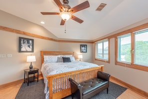 A bedroom with a wooden bed, a bench, a ceiling fan, and large windows.