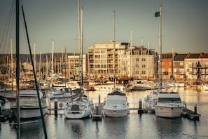 A marina with multiple boats docked, a building with balconies, and a clear sky.