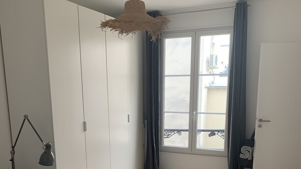 A bedroom with a bed, wardrobe, and a window with curtains.
