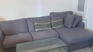 A living room with a grey sofa, a glass coffee table, and a grey carpet.