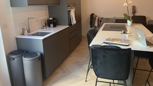 A modern kitchen with a sink, coffee maker, and a dining area with a laptop and chairs.