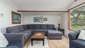 Un salon moderne avec un canapé d’angle gris, une table basse en bois et des tableaux encadrés accrochés au mur.