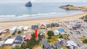 Vue aérienne d’une zone résidentielle côtière, avec des maisons, une plage et un promontoire rocheux dans la mer.