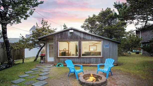 Une petite cabane avec un foyer et deux chaises Adirondack bleues dans la cour.