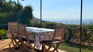 Un porche techado con una mesa y sillas, con vistas a la costa.