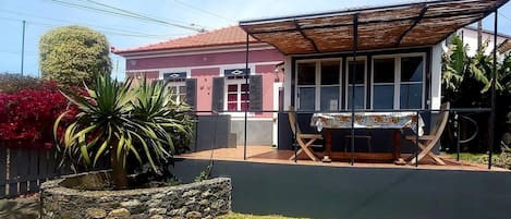 Uma casa com varanda coberta, um floreiro de pedra e um pequeno gramado.