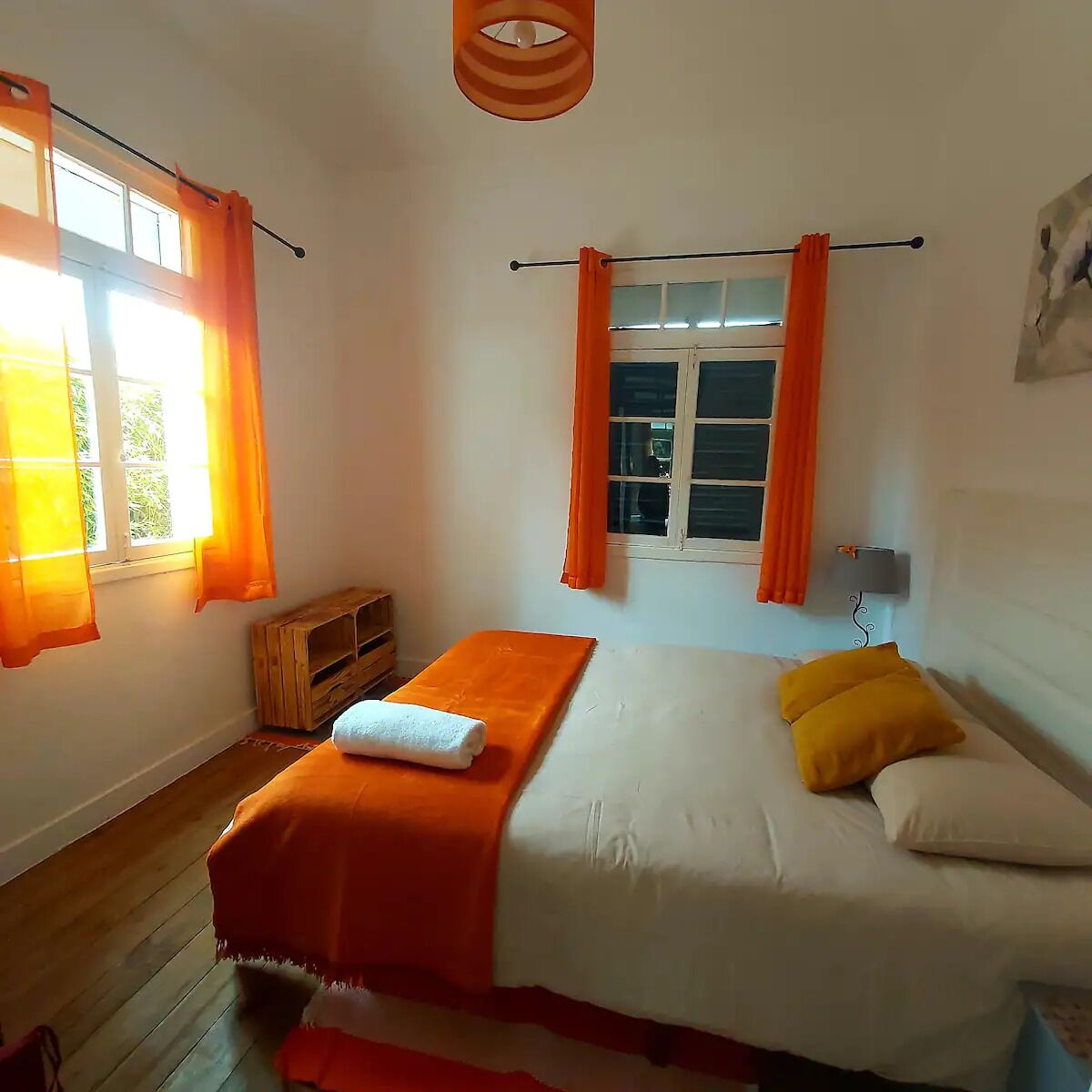 A bedroom with a bed, orange curtains, a wooden bench, and a wall-mounted lamp.