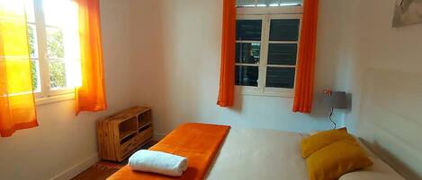 A bedroom with a bed, orange curtains, a wooden bench, and a wall-mounted lamp.