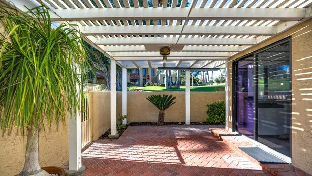 A covered patio area with a brick floor, a potted plant, and a view of the street. - Corsican Villas 2BD Condo- Near Living Desert (Palm Desert)