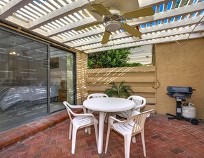 Eine Terrasse mit einem runden Tisch, weißen Plastikstühlen, einem Deckenventilator und einem Grill.