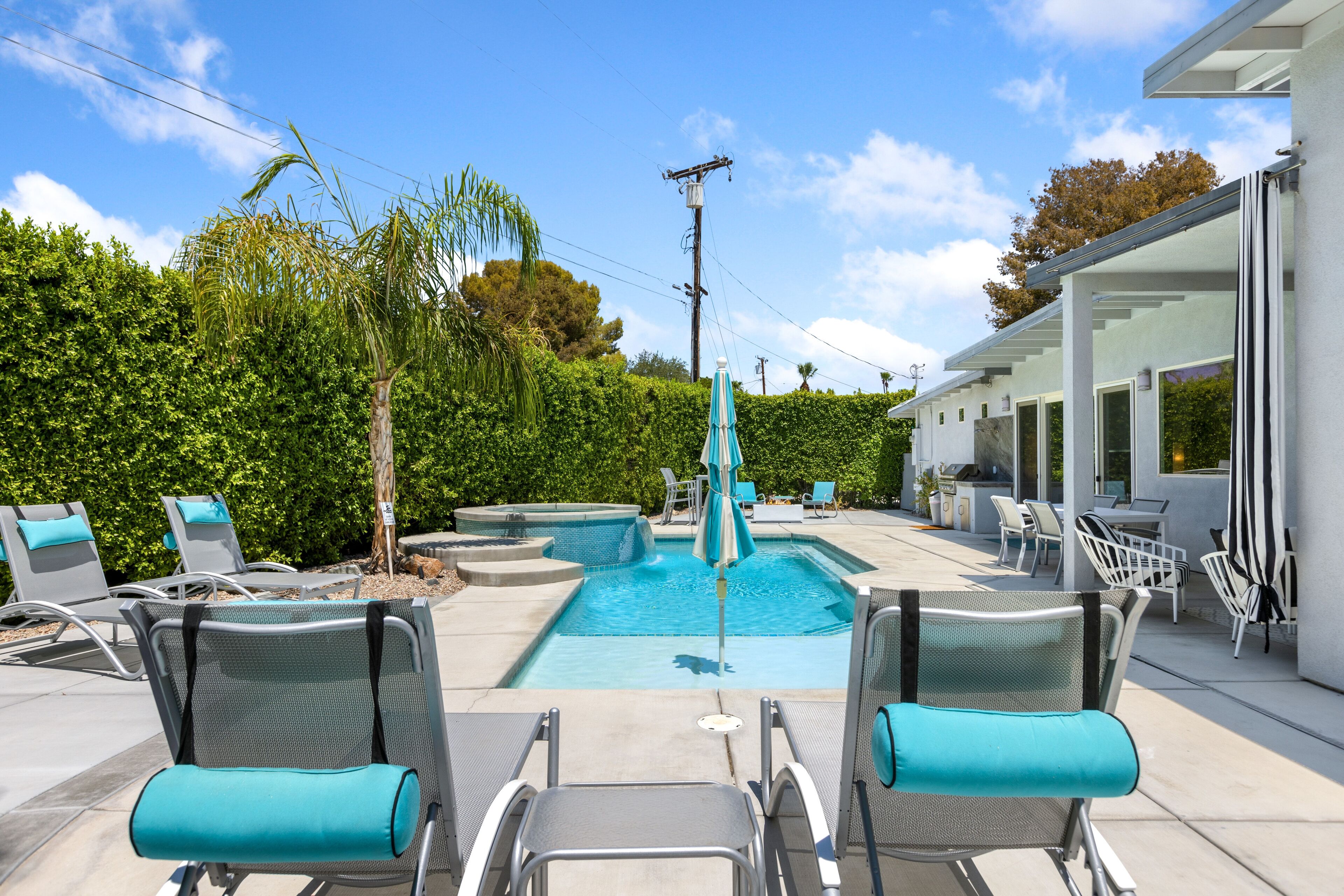 A pool area with lounge chairs, a hot tub, and umbrellas.