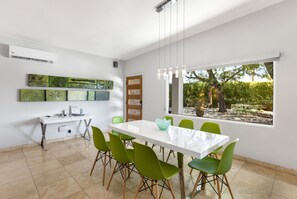 A modern dining area with a white table and green chairs, a whiteboard, and artwork on the wall.
