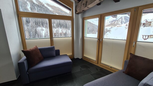 A corner room with a sofa and a window with a view of a snowy mountain.