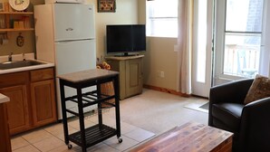 Un espacio habitable compacto con kitchenette, televisor, mesa de comedor y sofá.