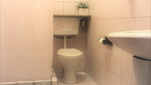 Une petite salle de bain compacte, équipée de toilettes, d’un lavabo et d’une étagère sur laquelle est posée une plante.