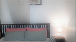 Un lit avec une couvre-lit à rayures et des oreillers, une table de chevet avec une lampe et un cadre photo fixé au mur.