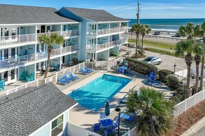 A multi-story hotel with a swimming pool, outdoor seating, and a view of the ocean.