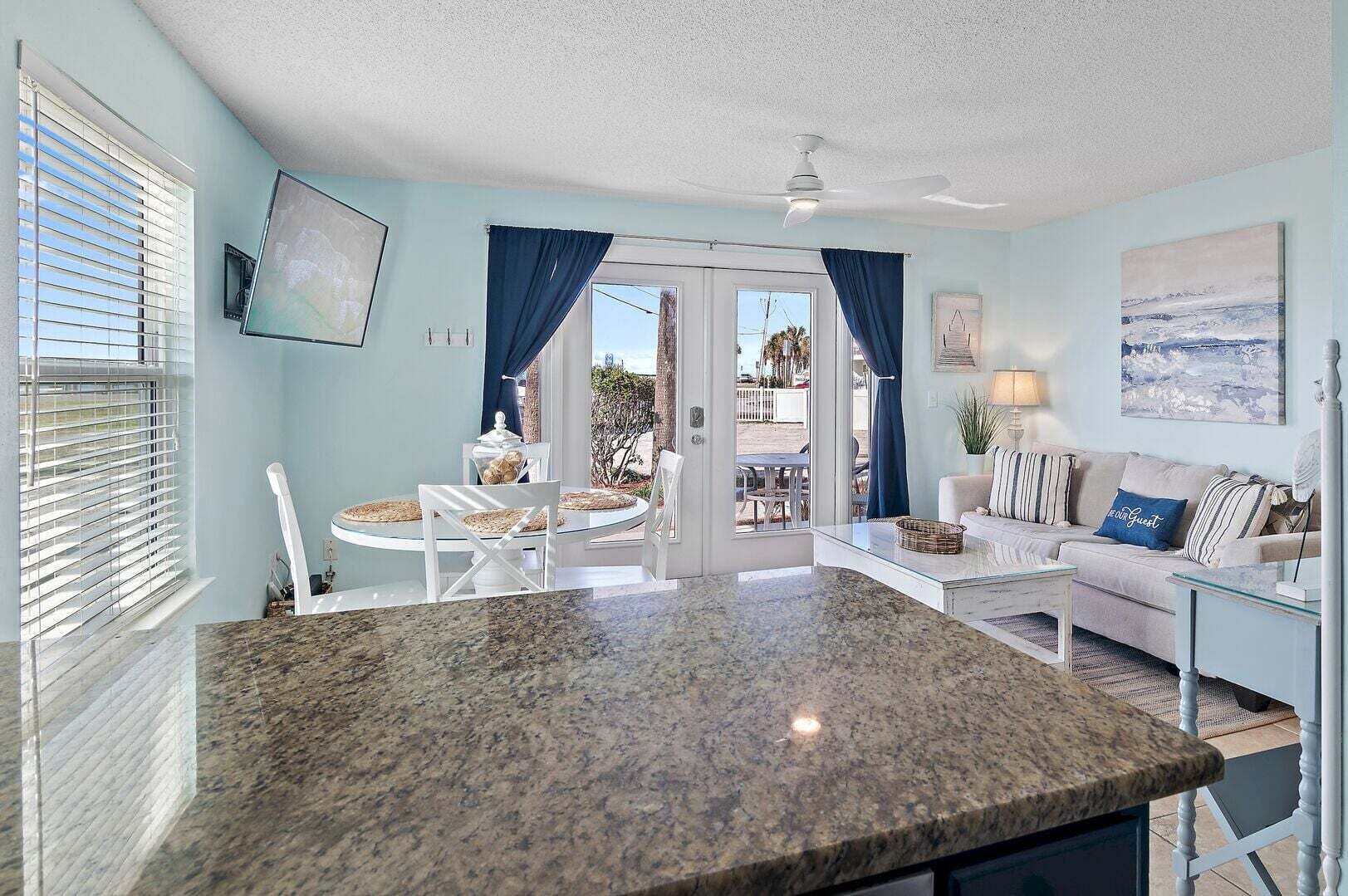 Un salón amplio con una isla grande de granito, un sofá con cojines a rayas, una mesa de comedor con sillas y vistas a un patio exterior a través de un ventanal.