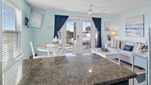 A spacious living area with a large granite island, a sofa with striped cushions, a dining table with chairs, and a view through a glass door to an outdoor patio. - 🌊Ground Floor | Beach Front | Upscale + Disc. Beach Service-Beach Blessing🌊 (Miramar Beach)