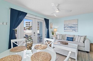 A room with a dining table, chairs, a sofa, a ceiling fan, and a view of the outside.