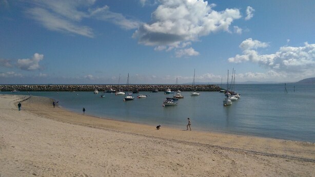 Una playa con barcos anclados cerca de un rompeolas rocoso.