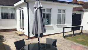 Un patio con una mesa redonda y sillas, una sombrilla gris y un edificio blanco con ventanas y una puerta.