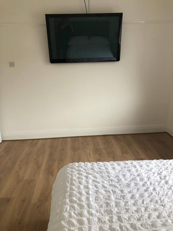 A bedroom with a bed, a wall-mounted TV, and wooden flooring.
