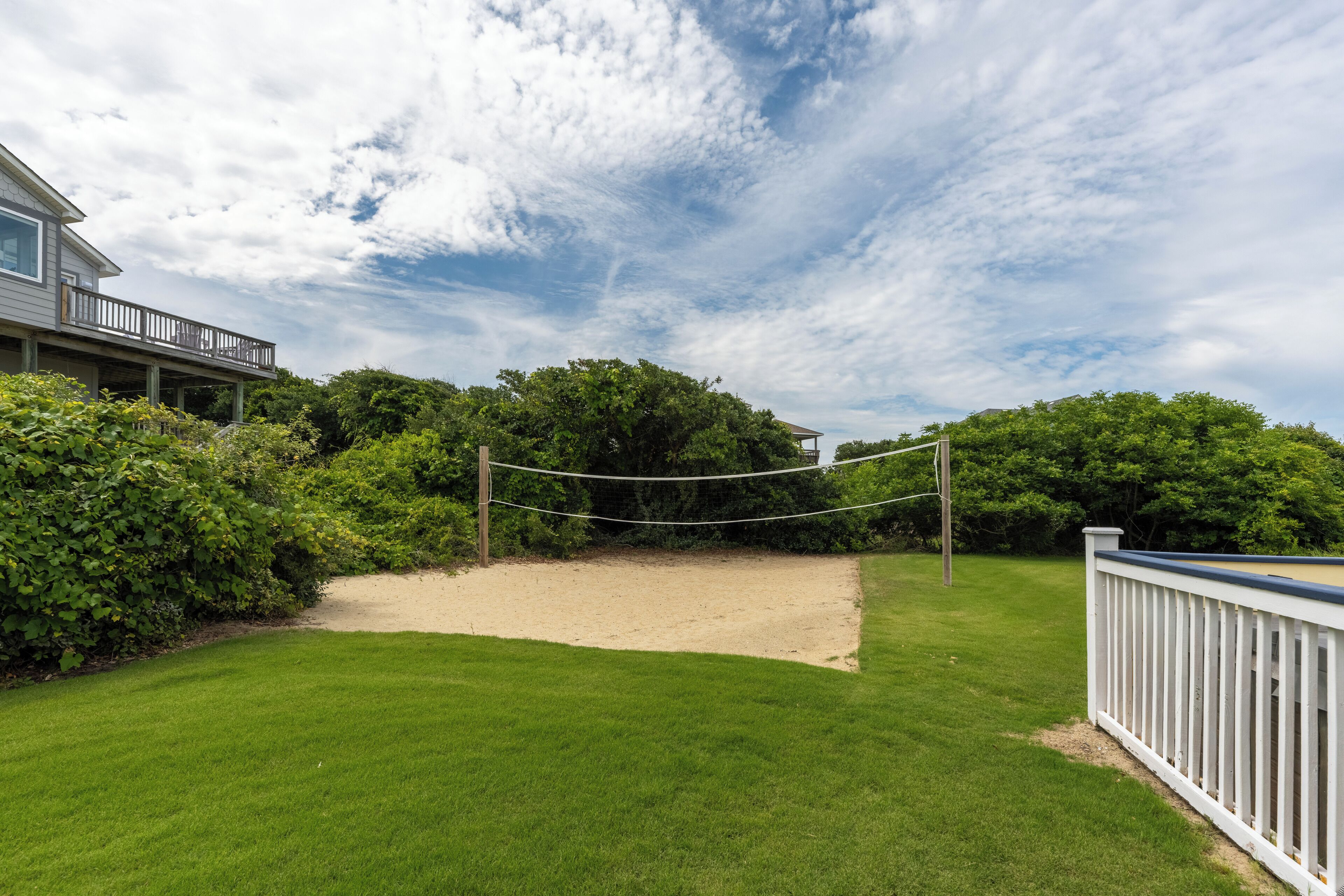 A well-maintained backyard with a volleyball net, a sandy area, and lush greenery.